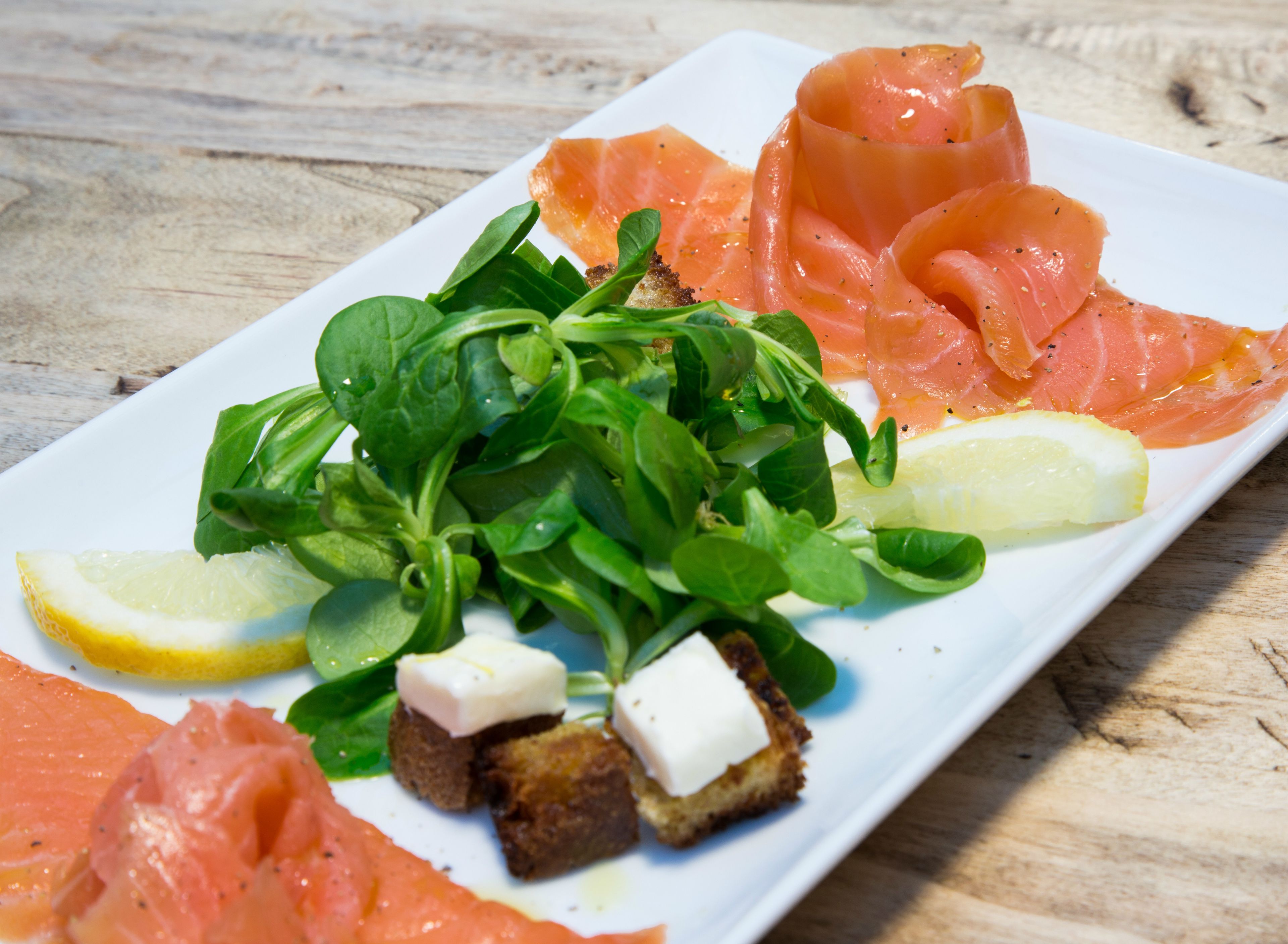 A plate of food with smoked salmon, greens, lemon, and cheese.