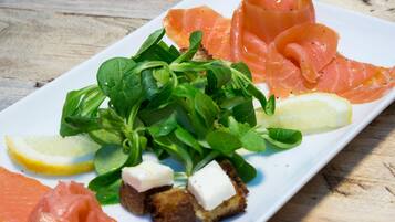 A plate of food with smoked salmon, greens, lemon, and cheese.