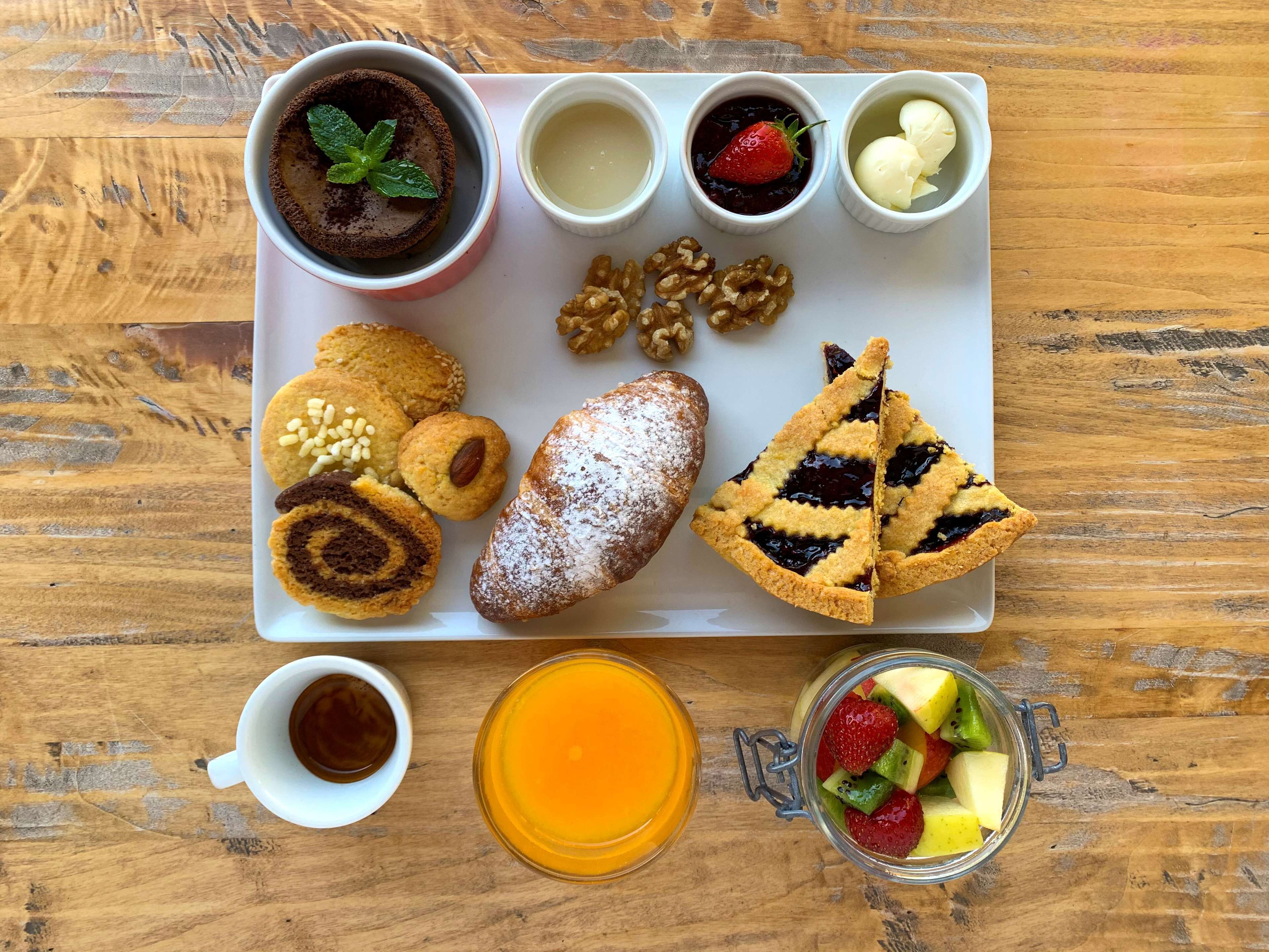 A tray with various pastries, a cup of coffee, a glass of orange juice, and a jar of mixed fruit.