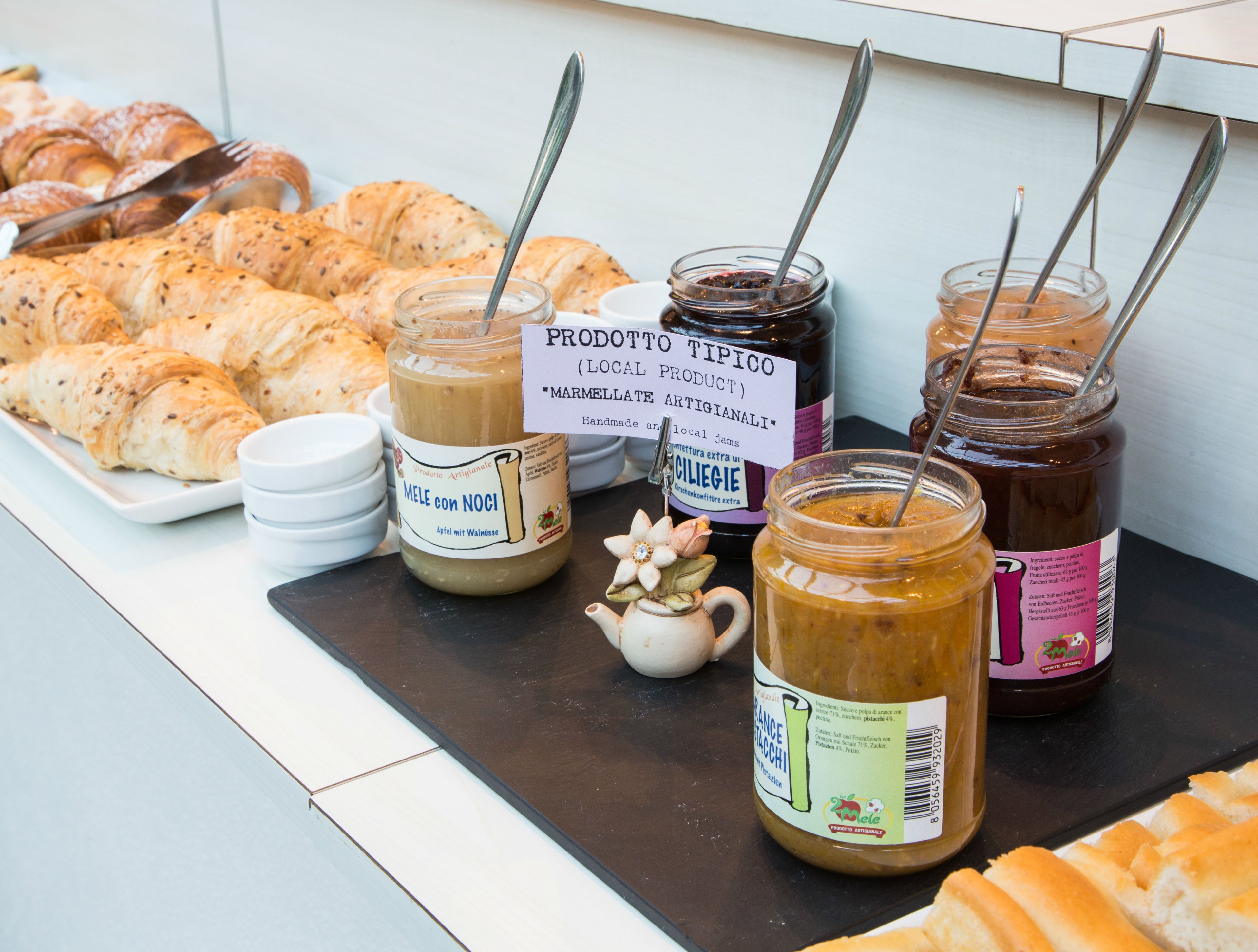 Un buffet de petit-déjeuner proposant des croissants, des confitures et un panneau indiquant les produits artisanaux locaux.