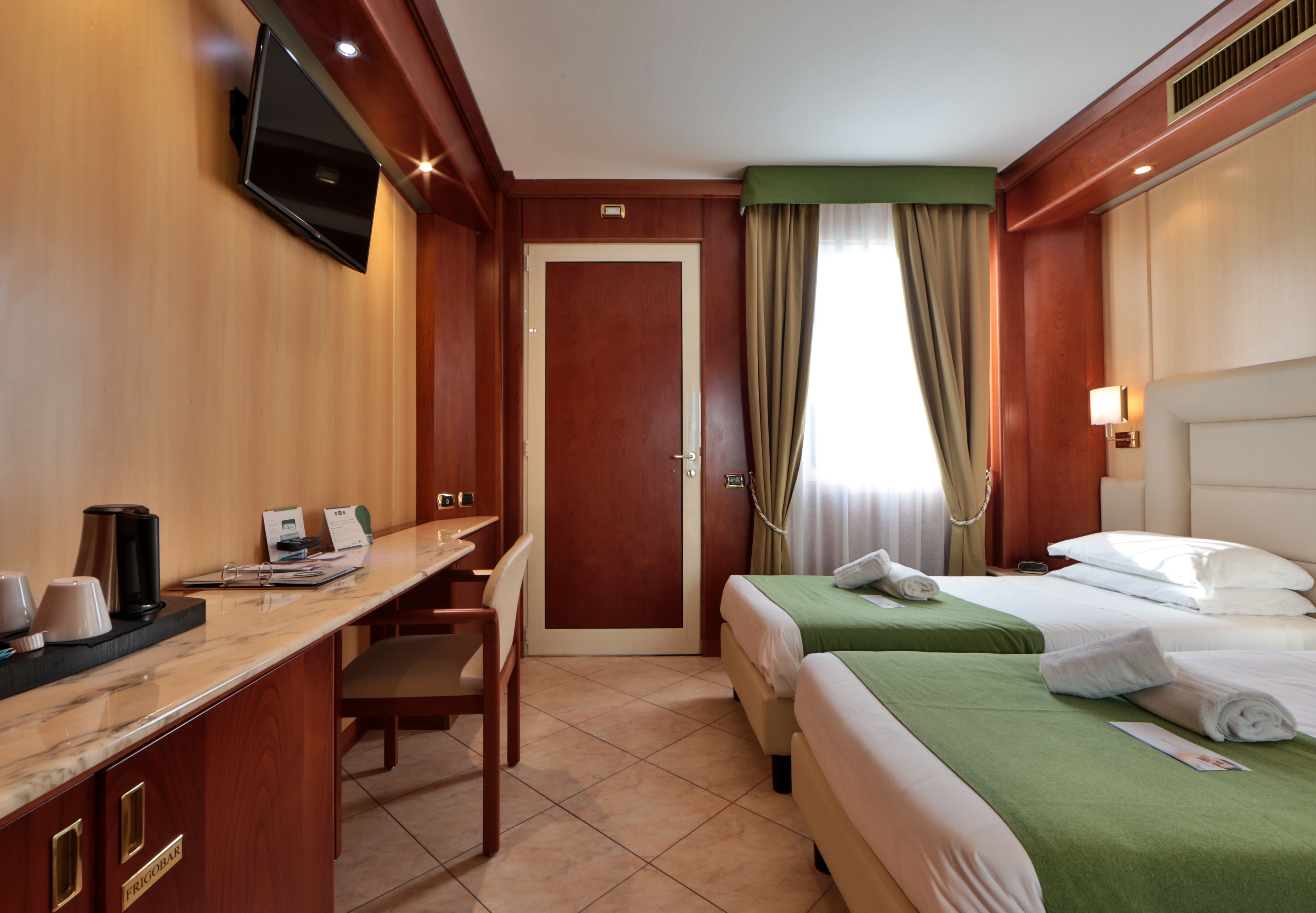 Una habitación de hotel con escritorio, dos camas, televisor y minibar.
