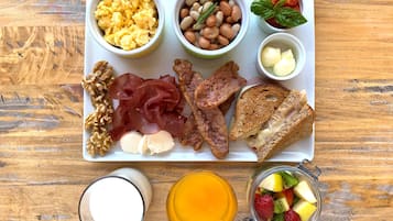 A breakfast tray with scrambled eggs, beans, tomatoes, basil, ham, cheese, toast, walnuts, prosciutto, and a fruit bowl.