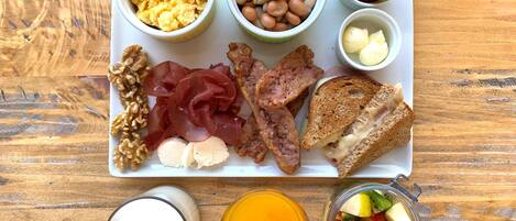 A breakfast tray with scrambled eggs, beans, tomatoes, basil, ham, cheese, toast, walnuts, prosciutto, and a fruit bowl.