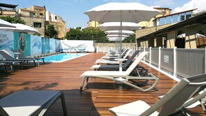 Un espace aménagé au bord de la piscine, avec des chaises longues et des parasols, une terrasse en bois et une piscine.