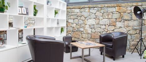 A modern living room with a stone wall, leather chairs, a wooden table, and a white shelving unit with plants.