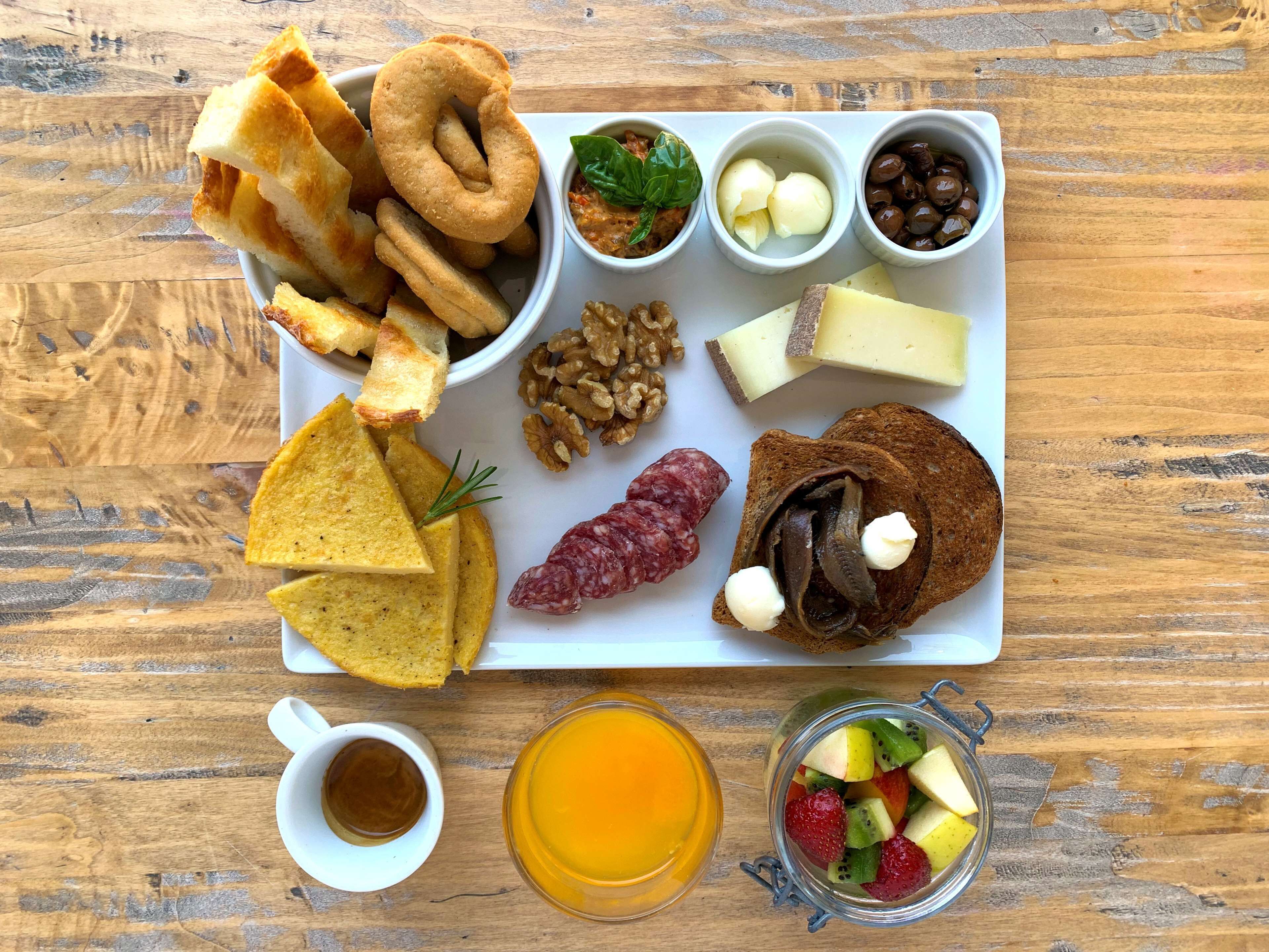 Ein Holztisch mit verschiedenen Speisen, darunter Brot, Käse, Nüsse und Obst.