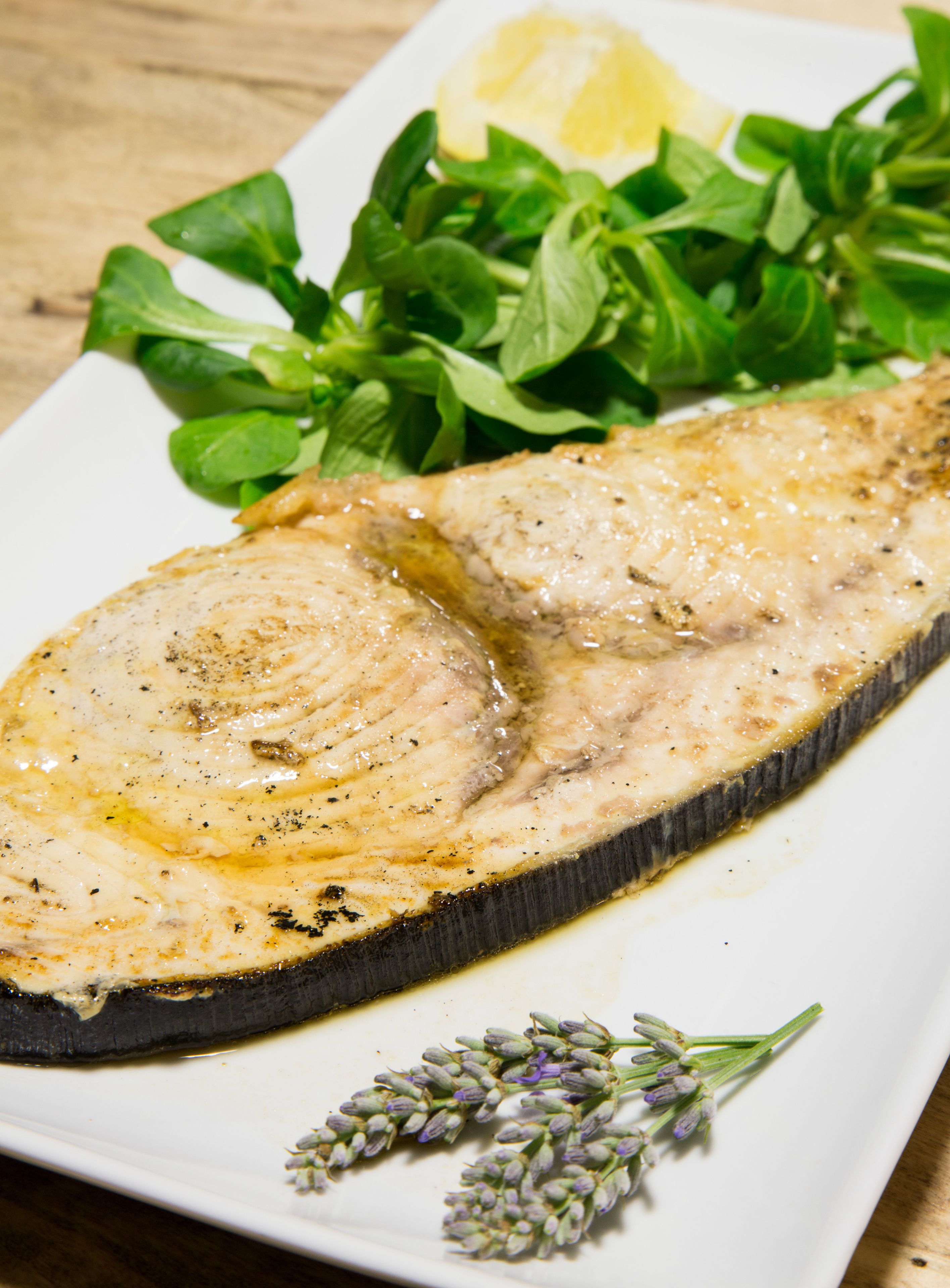 A plate with grilled fish, lemon, and green leaves.