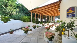 Un espace extérieur abrité, agrémenté de plantes en pot et d’une enseigne indiquant le Best Western Hotel Anthurium.