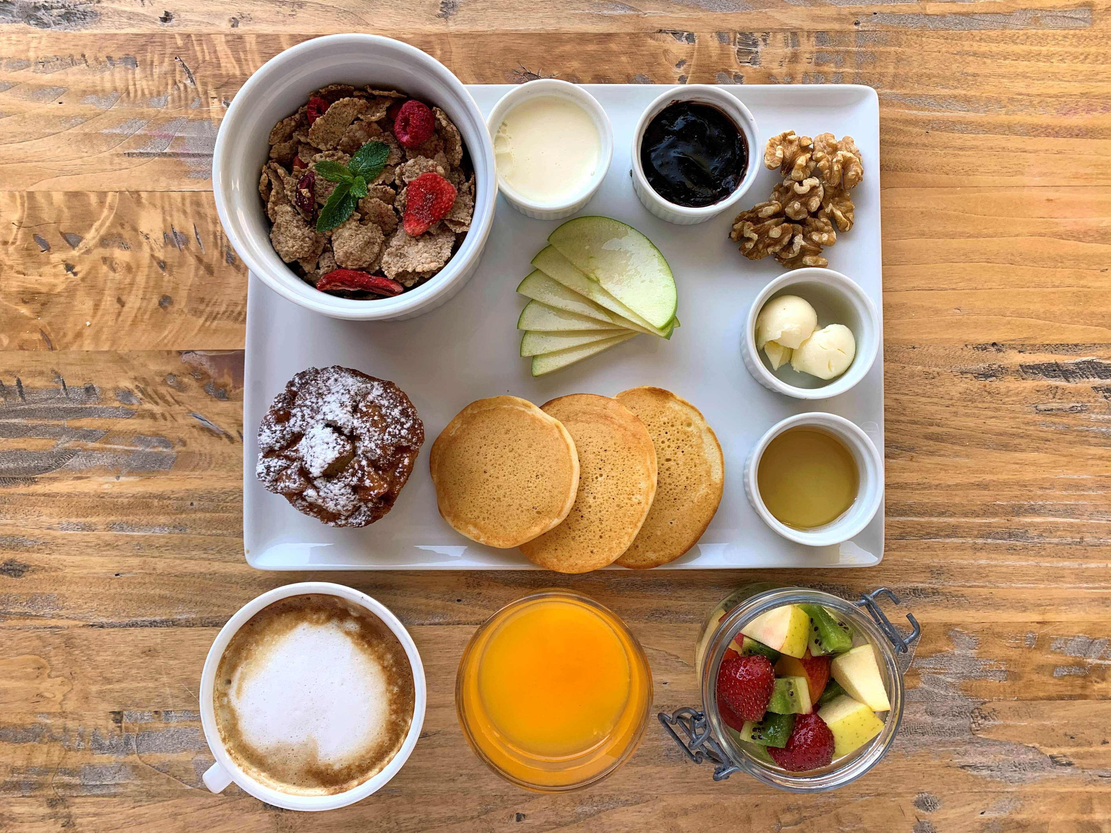 Ein Frühstücksbrett mit Pfannkuchen, einem Muffin, Obst und Getränken.