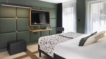 A modern hotel room with a large bed, a flat-screen TV mounted on a green padded wall, a small wooden side table, and a bench.
