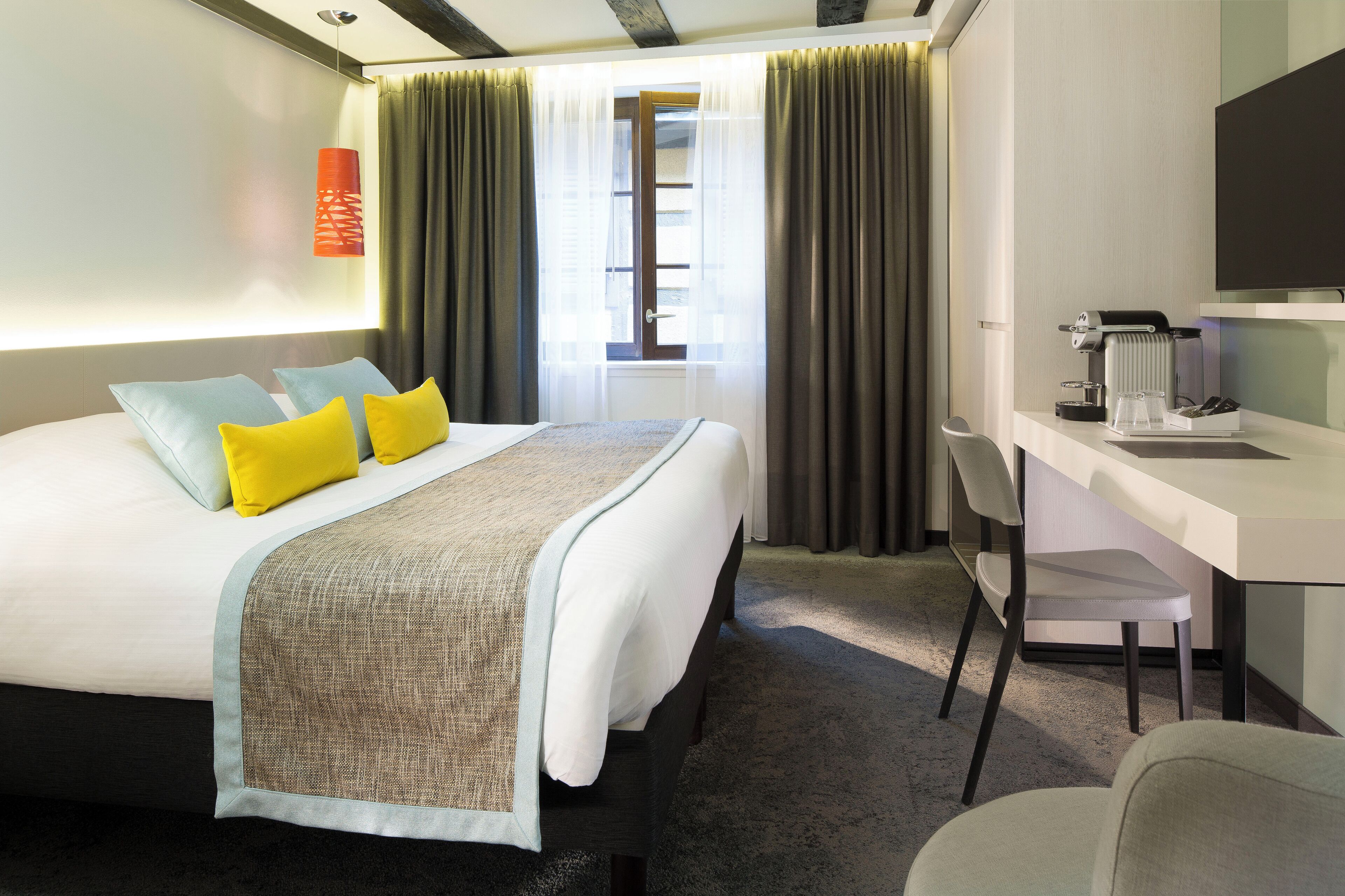 A hotel room with a bed, a desk, a chair, a television, and a window with curtains.