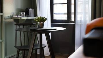 Ett rum med ett runt bord, två stolar, en krukväxt, en kaffemaskin och ett fönster med gardiner.
