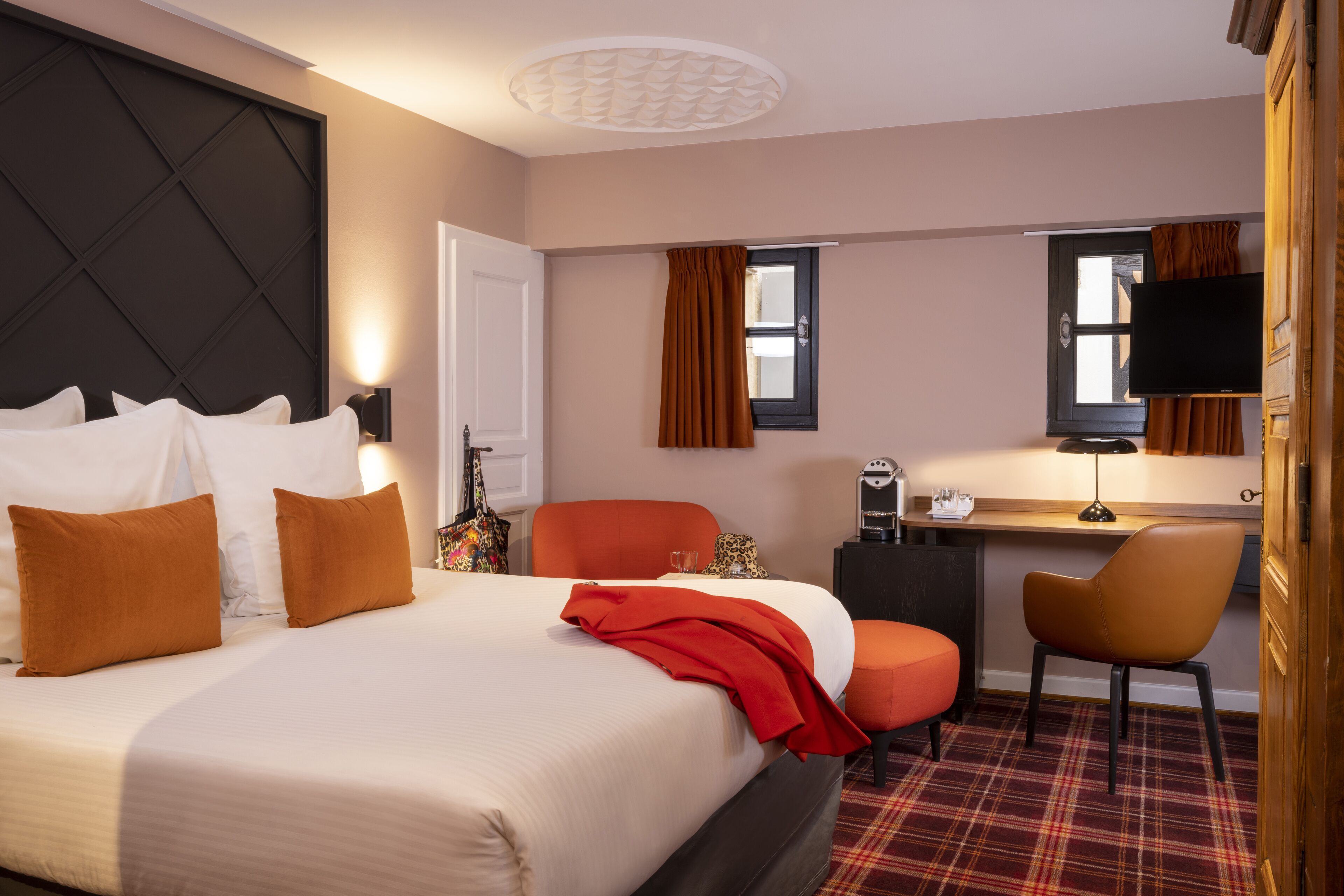 A hotel room with a large bed, a desk with a chair, a television, and a window with curtains.