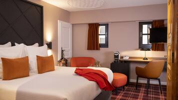 A hotel room with a large bed, a desk with a chair, a television, and a window with curtains.