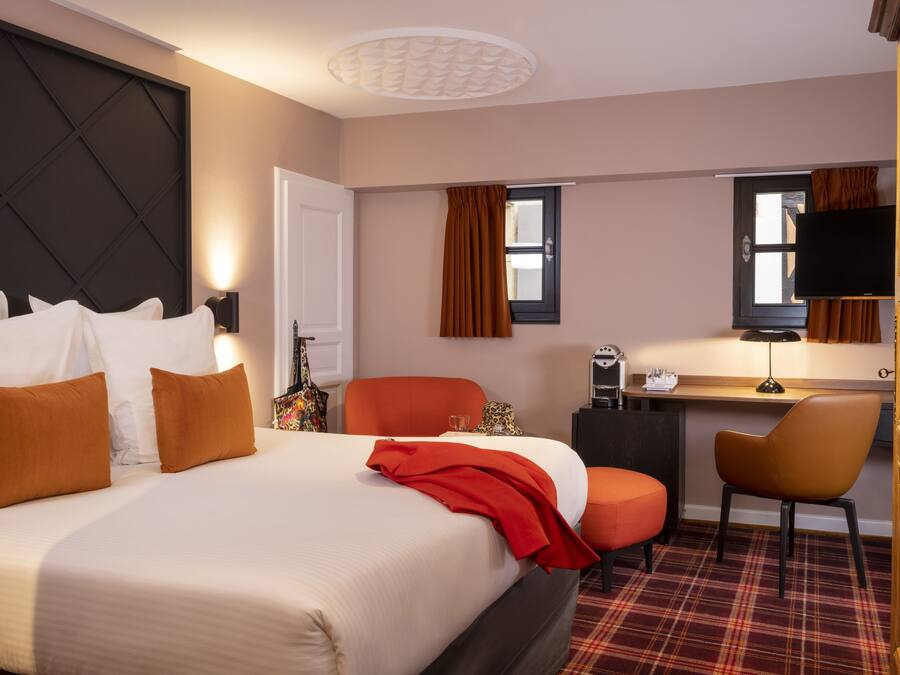 A hotel room with a large bed, a desk with a chair, a television, and a window with curtains.