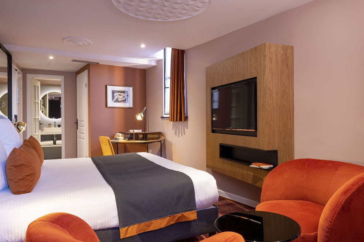 Hotellihuone, jossa on sänky, seinälle asennettu televisio, työpöytä ja tuoli.