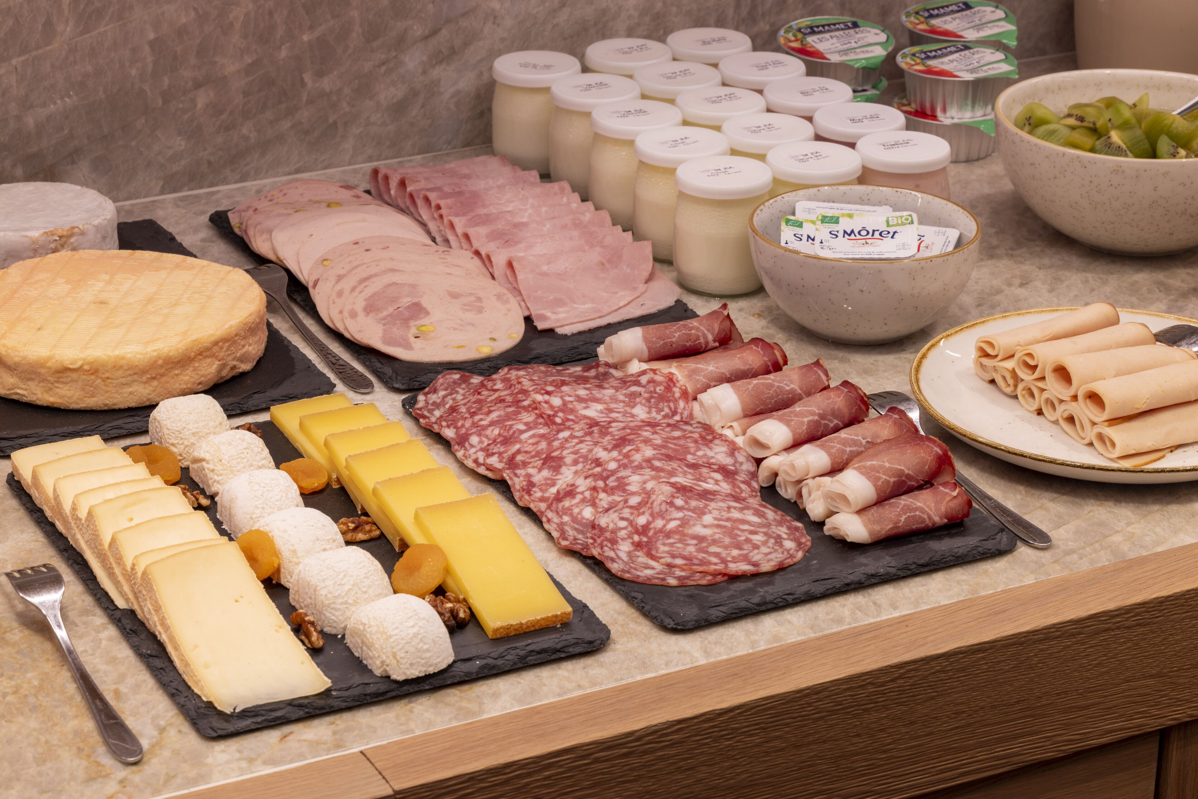 Une sélection de fromages, de charcuteries et de fruits secs présentés sur une planche en ardoise.