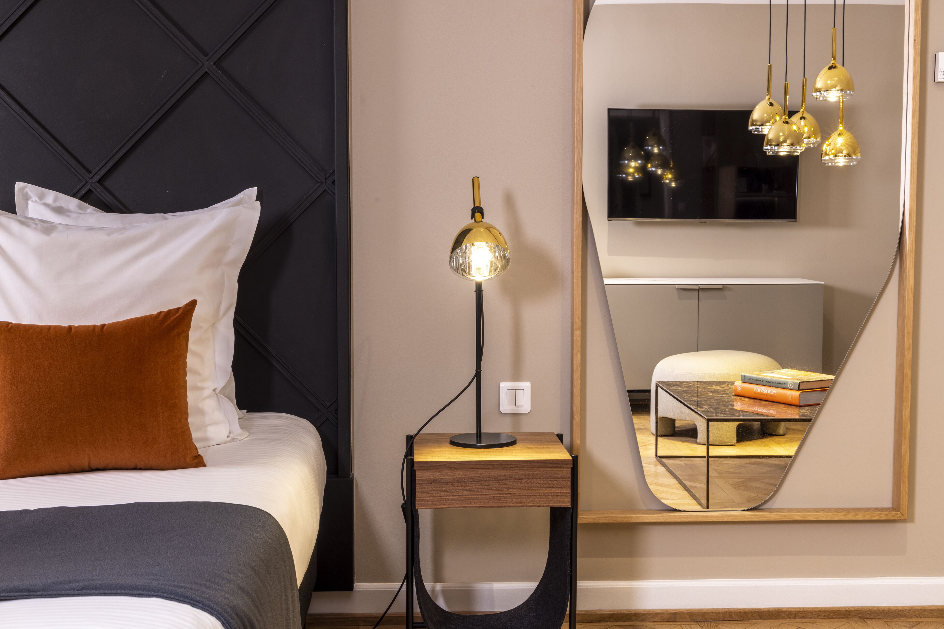 Quarto moderno com cama, mesa de cabeceira com luminária, espelho grande e televisão.