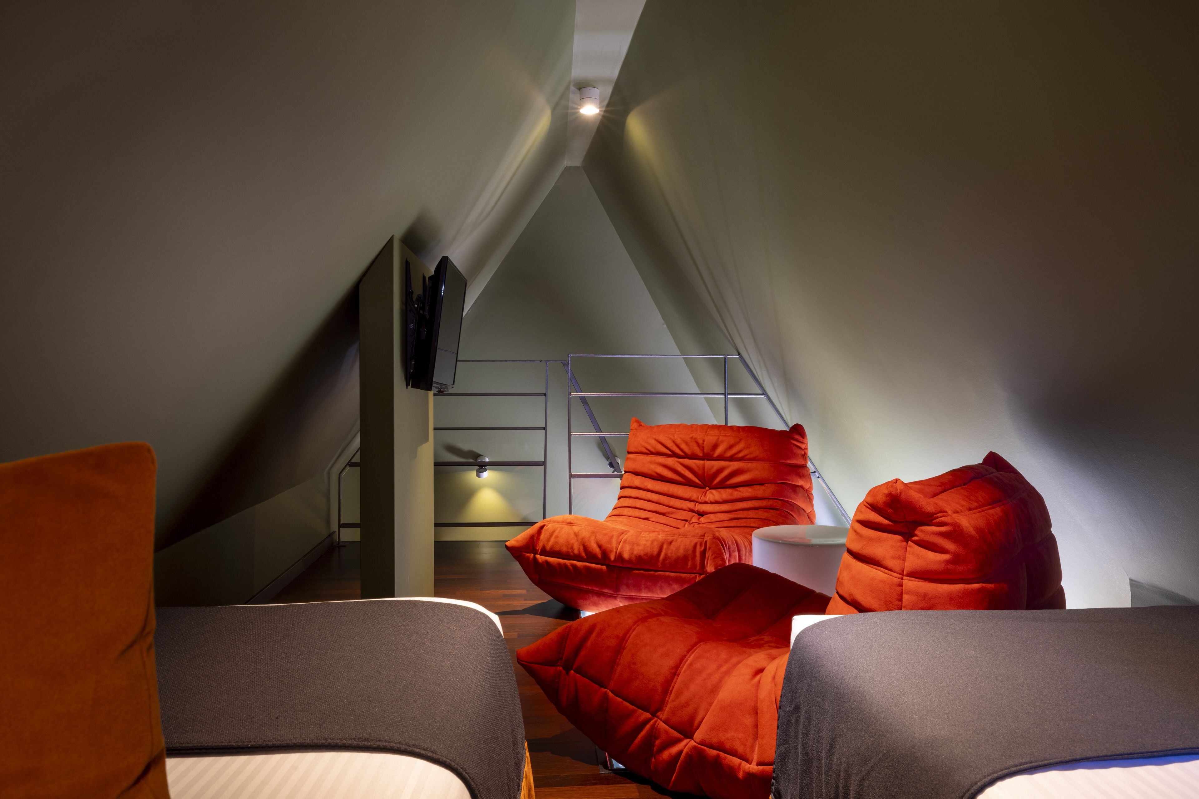 A cozy, modern loft bedroom with a sloped ceiling, a bed, and two red upholstered chairs.