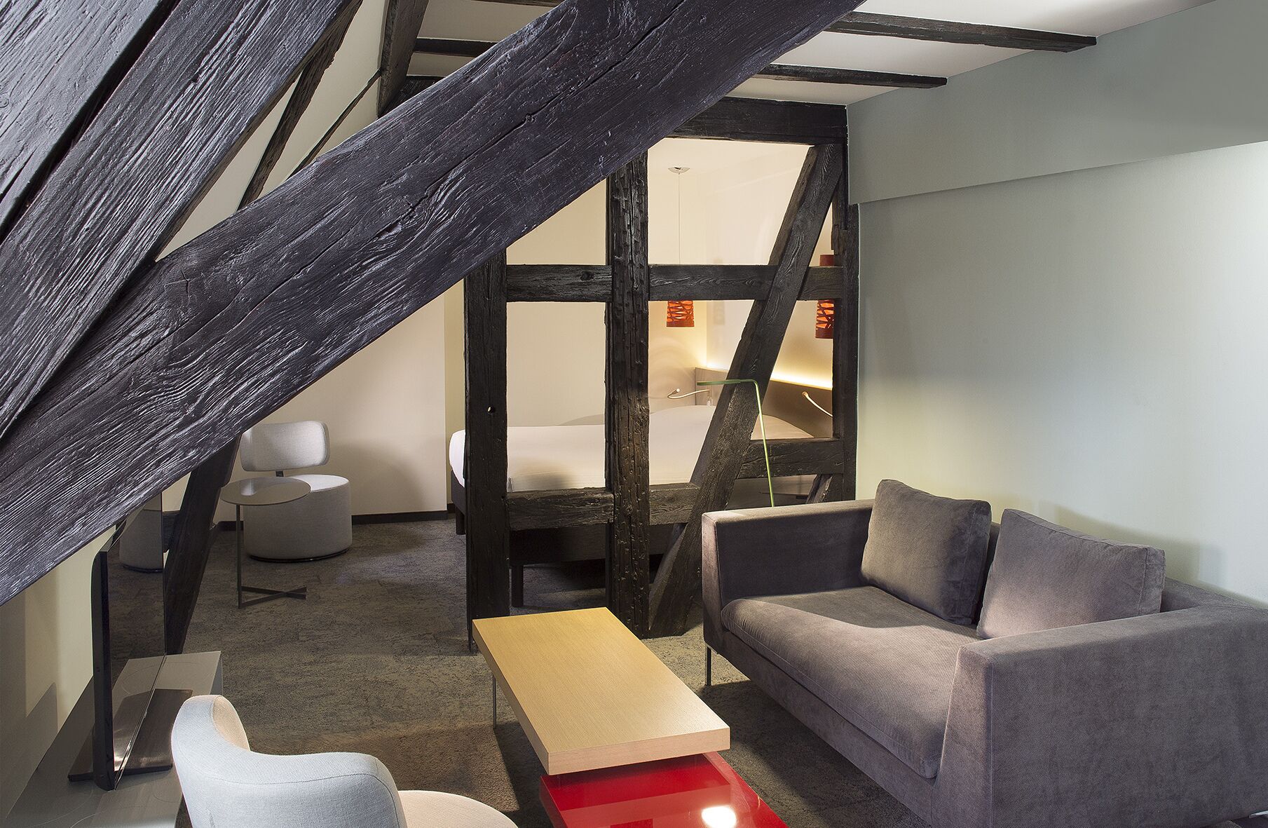 A modern room with a wooden ceiling, a grey sofa, a wooden coffee table, and a white chair.