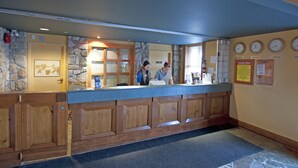 A reception desk with a stone wall backdrop, wooden cabinets, and clocks on the wall. - White Crystal Inn (Beaverdell)