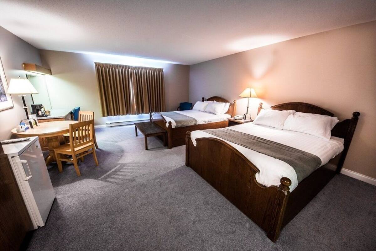 A hotel room with two single beds, a desk with a chair, a small fridge, and a window with curtains.