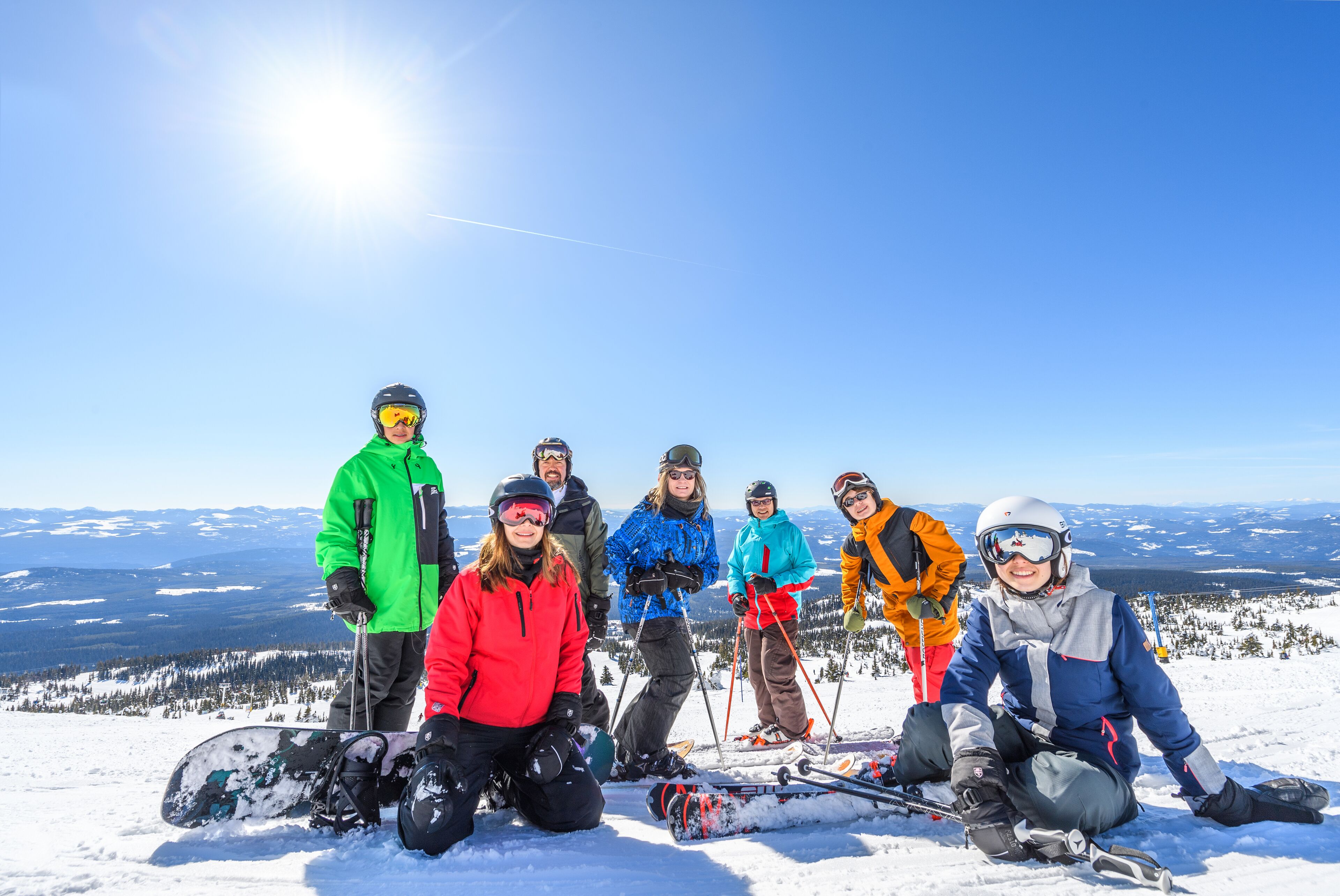 A group of people on a snowy mountain with ski equipment, standing and sitting on the snow.