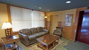 A living room with a brown leather sofa, a wooden coffee table, a side table with a lamp, and a patterned rug. - White Crystal Inn (Beaverdell)