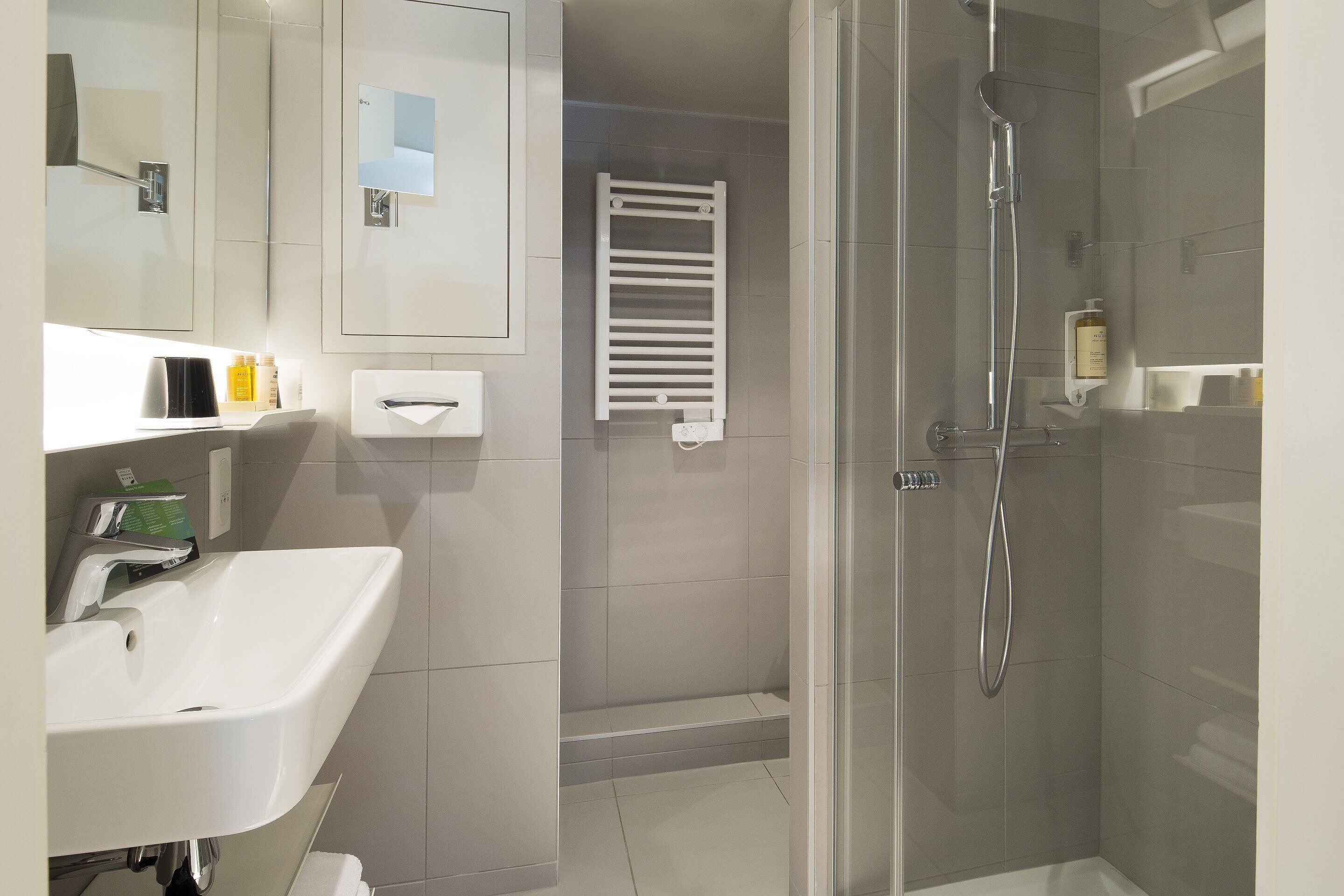 A modern bathroom with a white sink, mirror, and glass-enclosed shower.