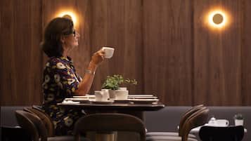 A person seated at a table with a cup, surrounded by chairs and a small plant.