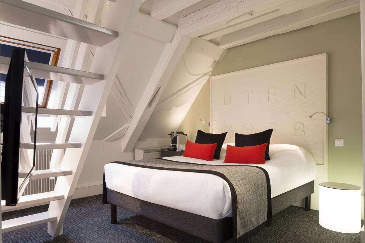 Un dormitorio moderno con cama estilo loft, una escalera y un gran cabecero fijado a la pared con la palabra "UTEN" a la vista.