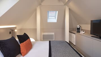 Habitación de hotel compacta con cama, kitchenette pequeña, televisor y ventana con vistas al exterior.