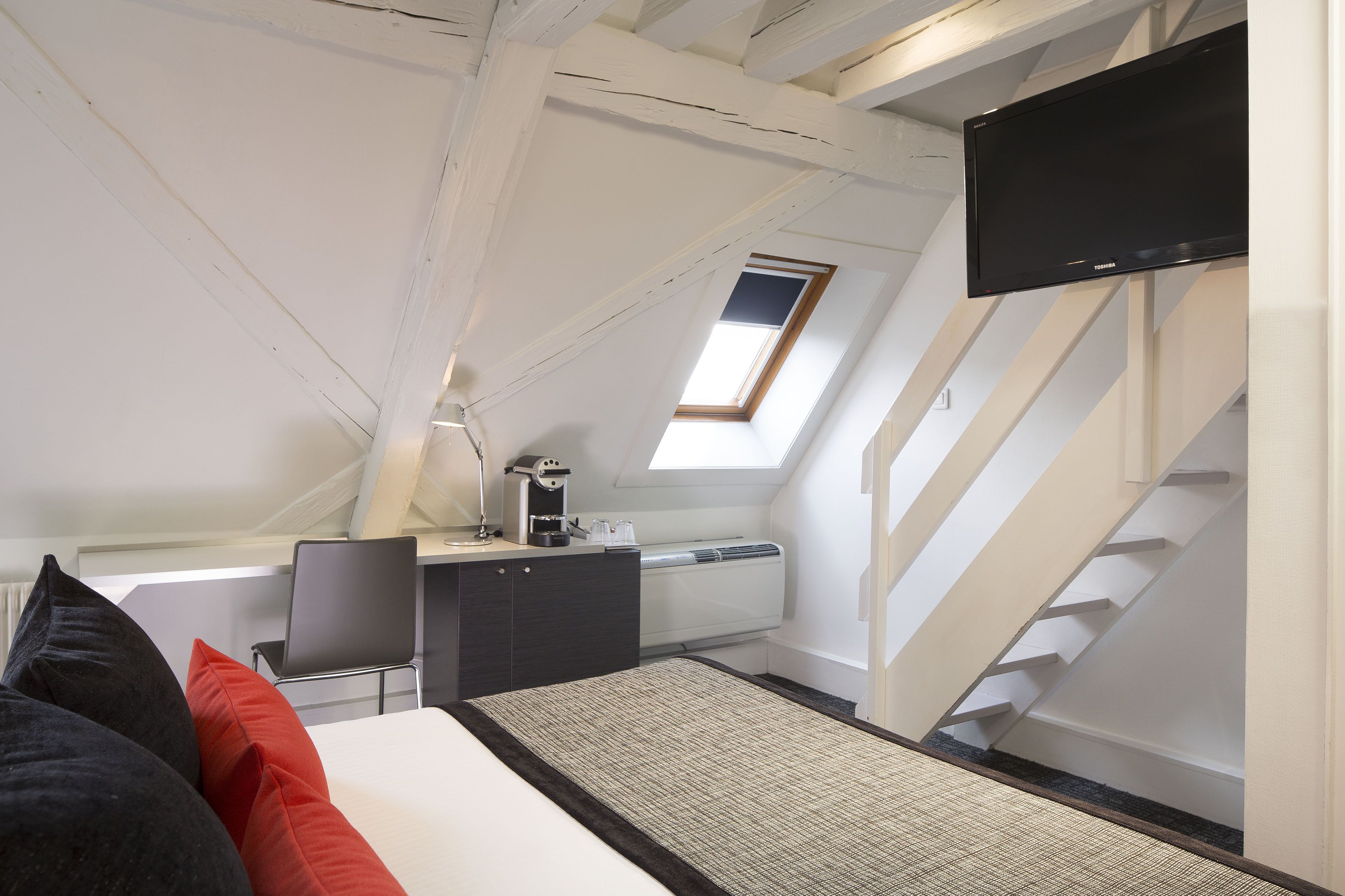 A bedroom with a bed, a desk, a chair, a TV, and a staircase.