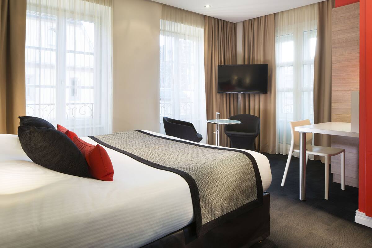 Una habitación de hotel con cama, escritorio, silla y televisión.