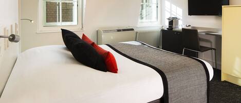 A hotel room with a large bed, a desk, a chair, a television, and a window.
