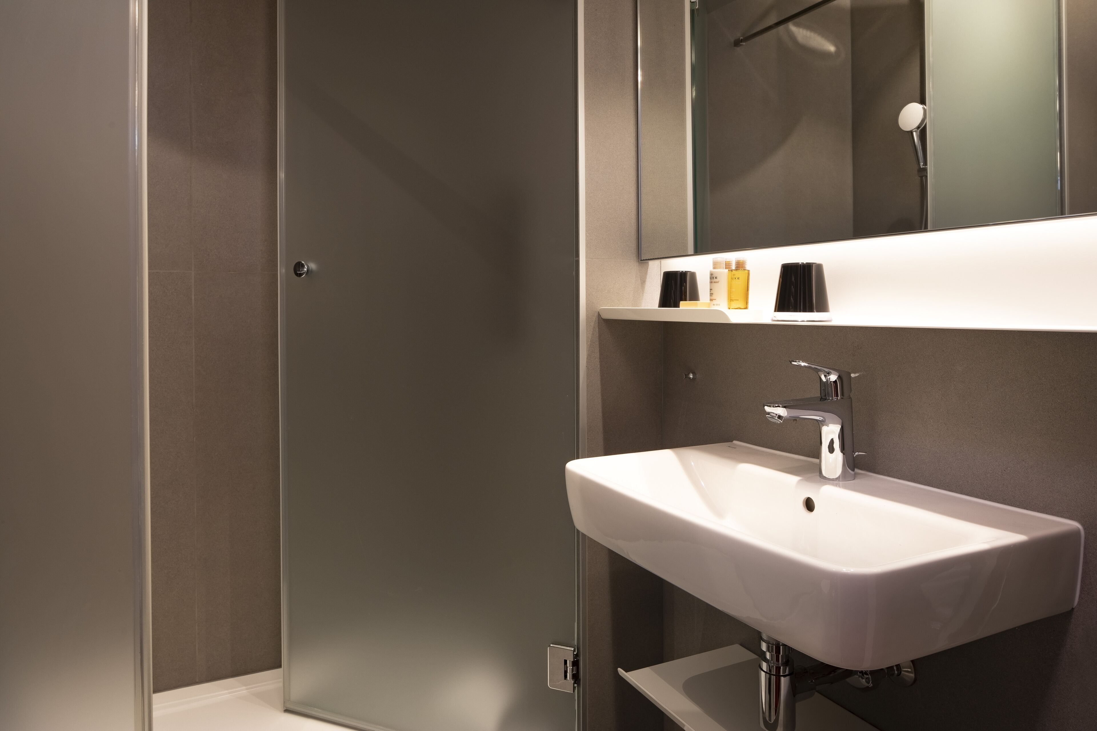 Un baño moderno con un lavamanos blanco, un espejo encima y una zona de ducha.