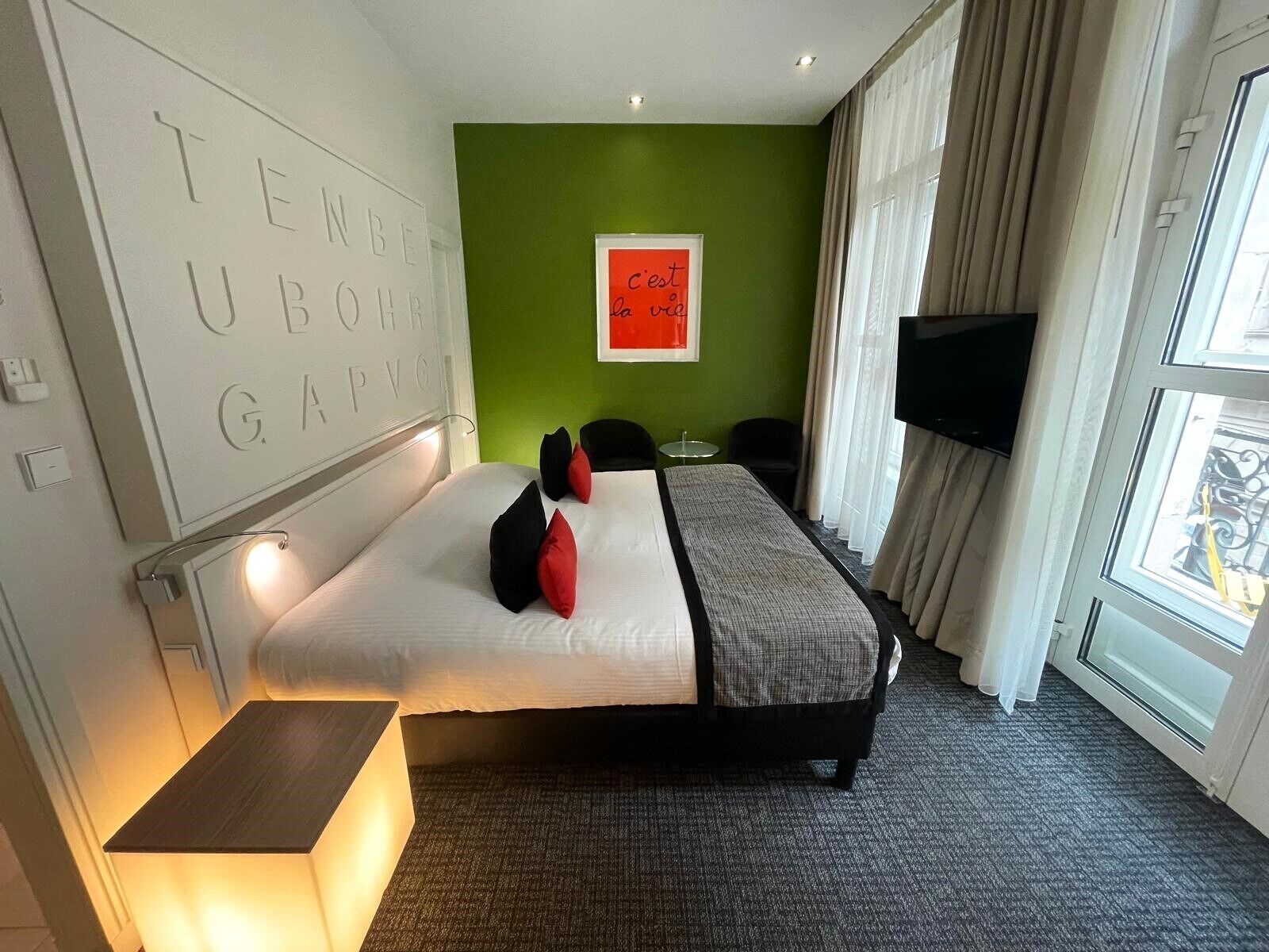 Ein Hotelzimmer mit Bett, Nachttisch, Fernseher und einer grünen Akzentwand.