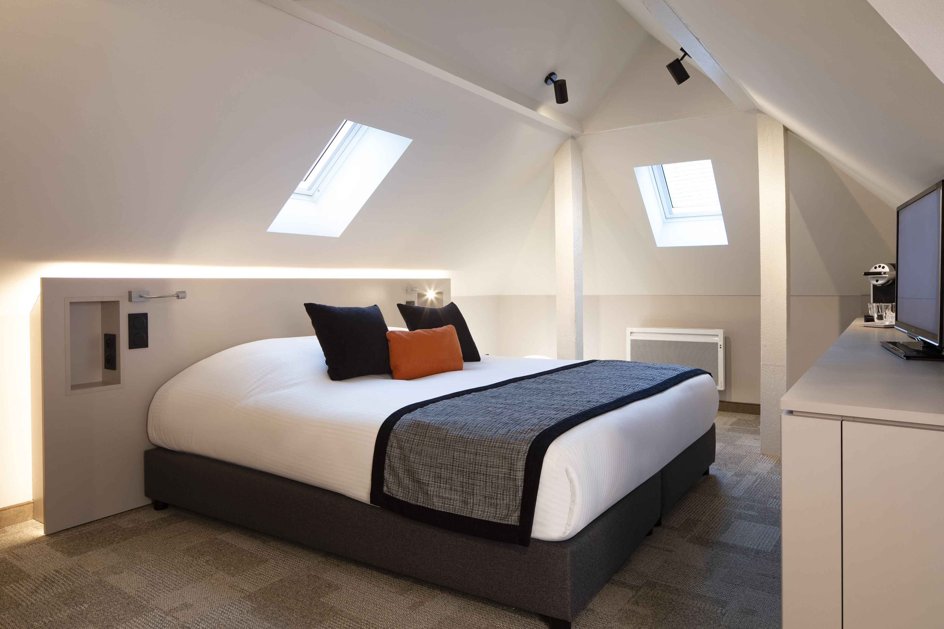 Un dormitorio moderno con una cama grande, dos tragaluces, un escritorio y un radiador.