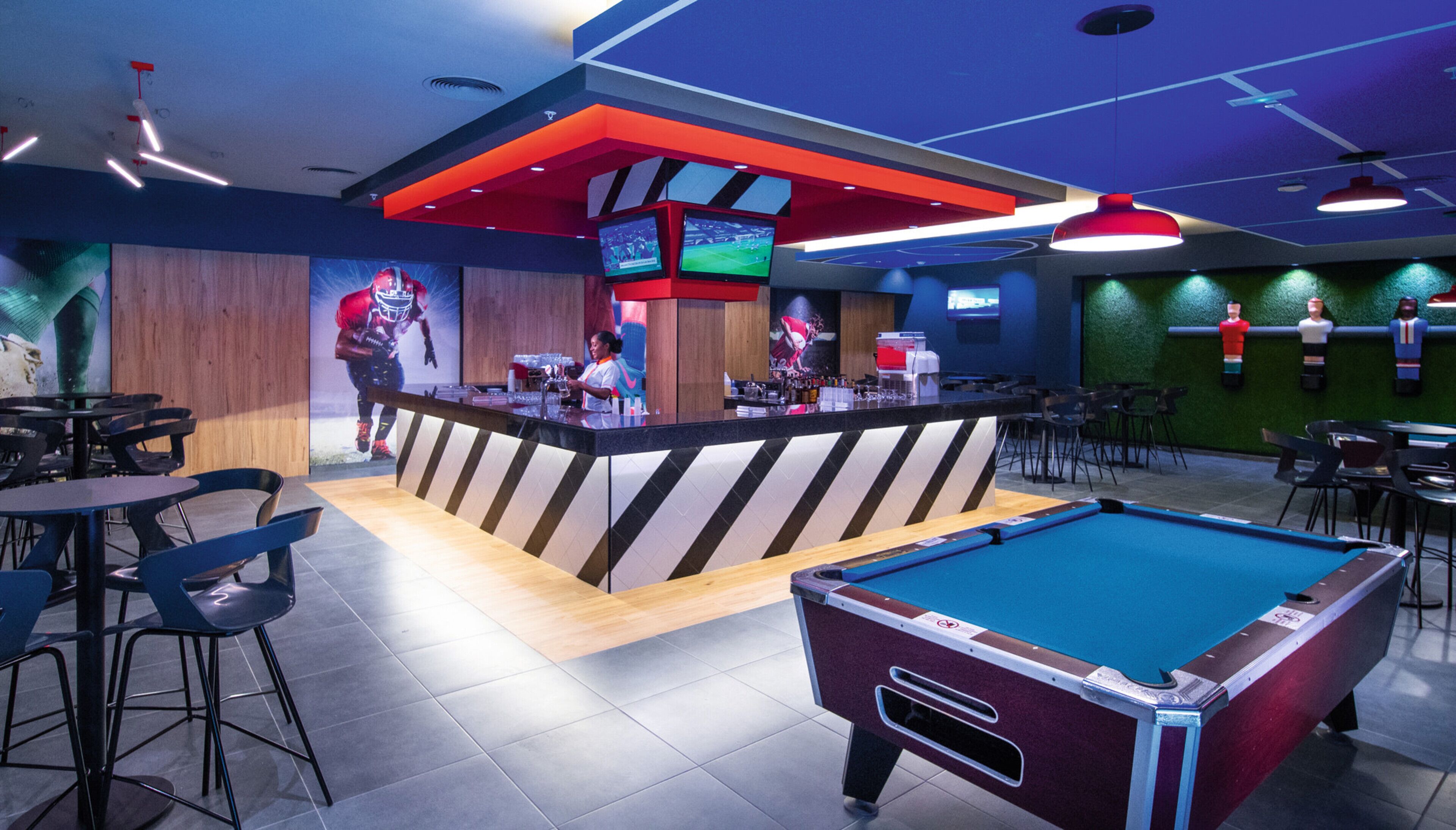 Uma área de bar com mesa de bilhar, banquetas e balcão com uma tela de televisão.