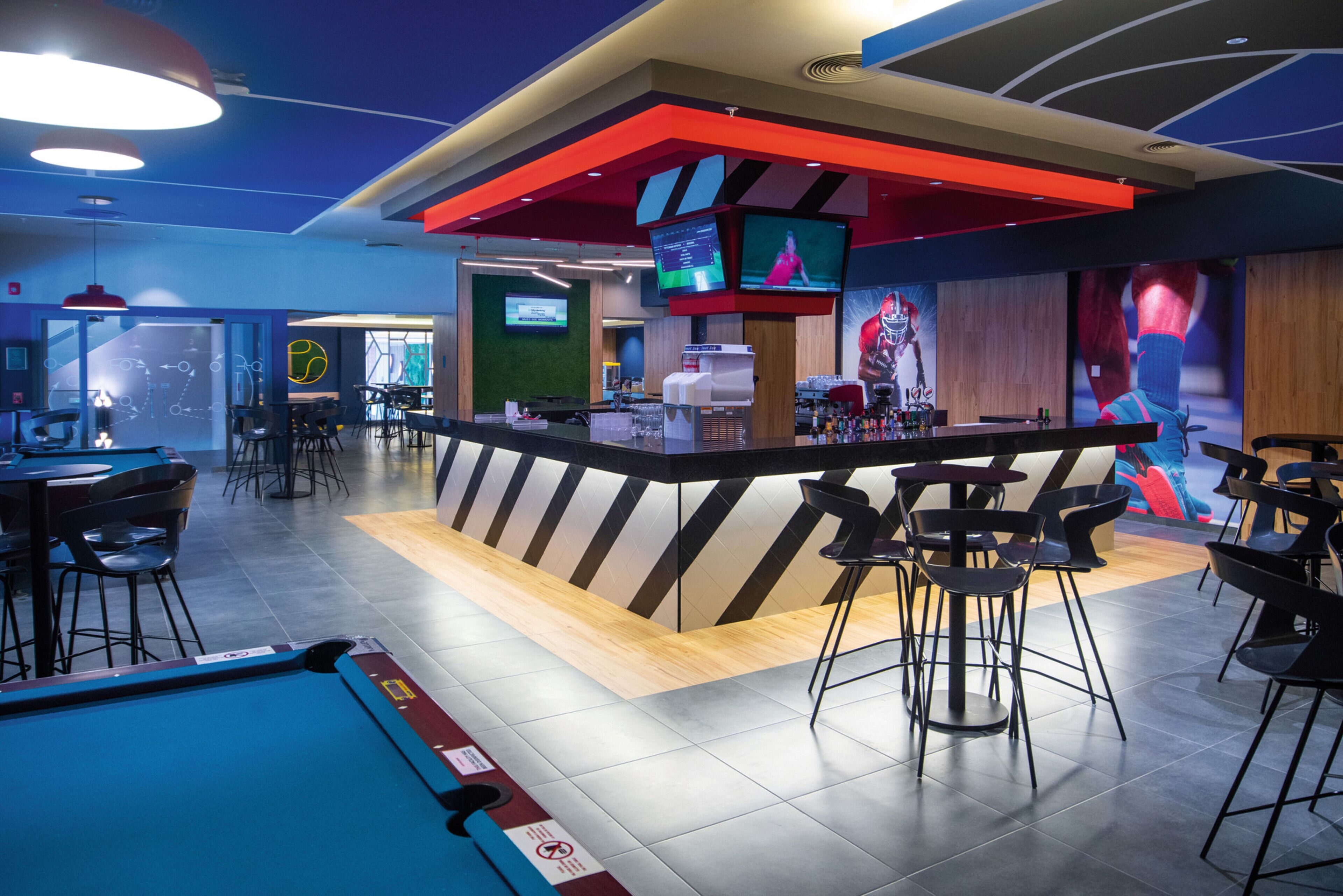 A modern bar area with a pool table, bar stools, and a counter with a TV screen.