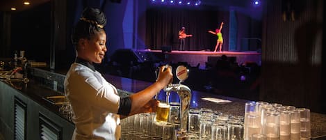 A bartender pouring a drink at a bar with a stage in the background.