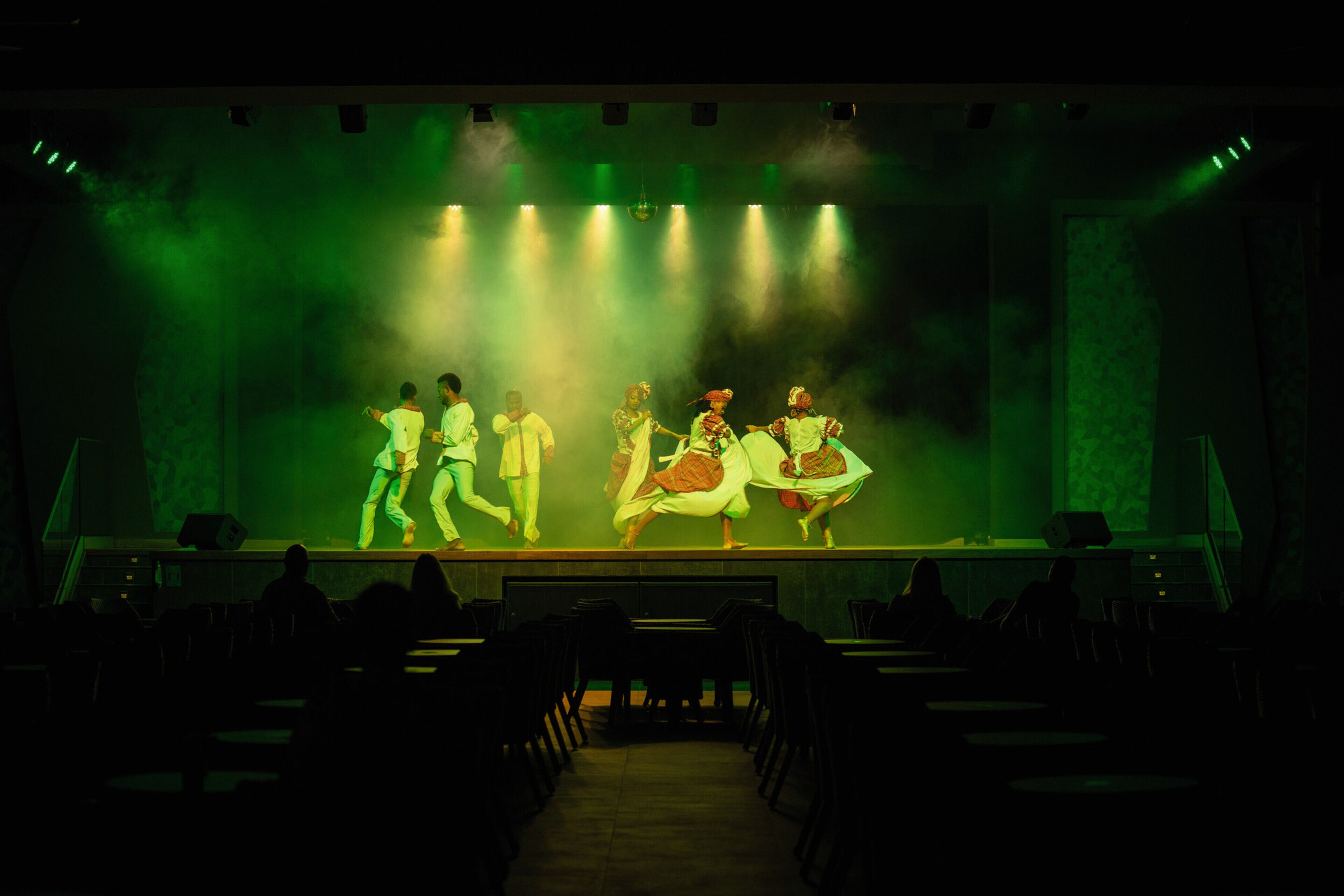 A stage with performers in traditional attire, a row of chairs facing the stage, and a smoke effect.