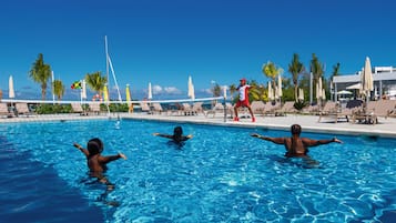 Una piscina con lettini e ombrelloni, circondata da palme e un cielo sereno.