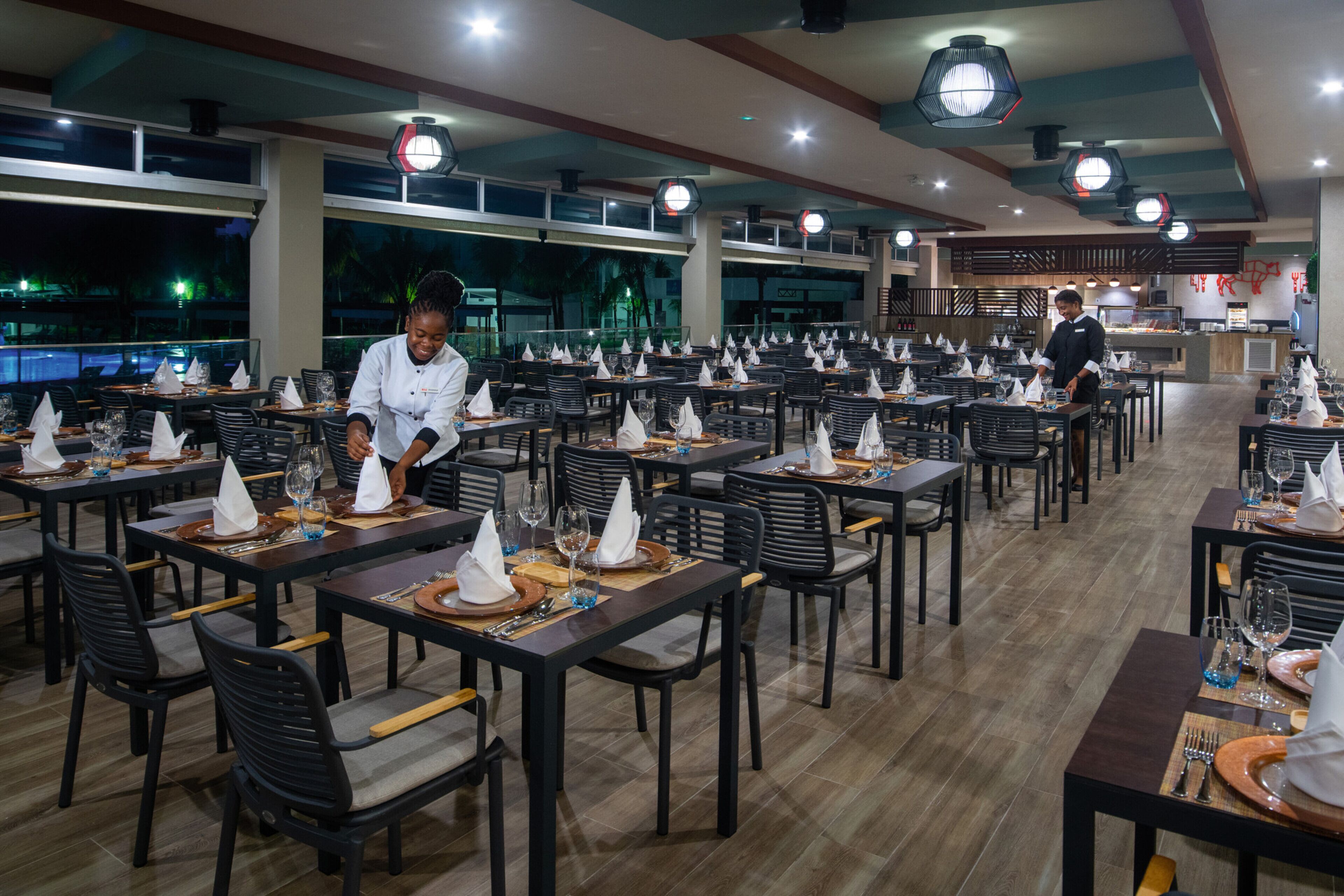 Een ruim restaurant met meerdere eettafels en stoelen, een bar en grote ramen met uitzicht op een zwembad.