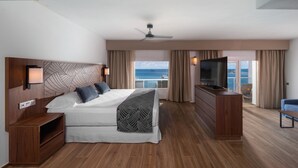 A modern hotel room with a large bed, a TV, a wooden dresser, and a balcony with a view of the ocean. - Hotel Riu Montego Bay - Adults Only - All Inclusive (Montego Bay)
