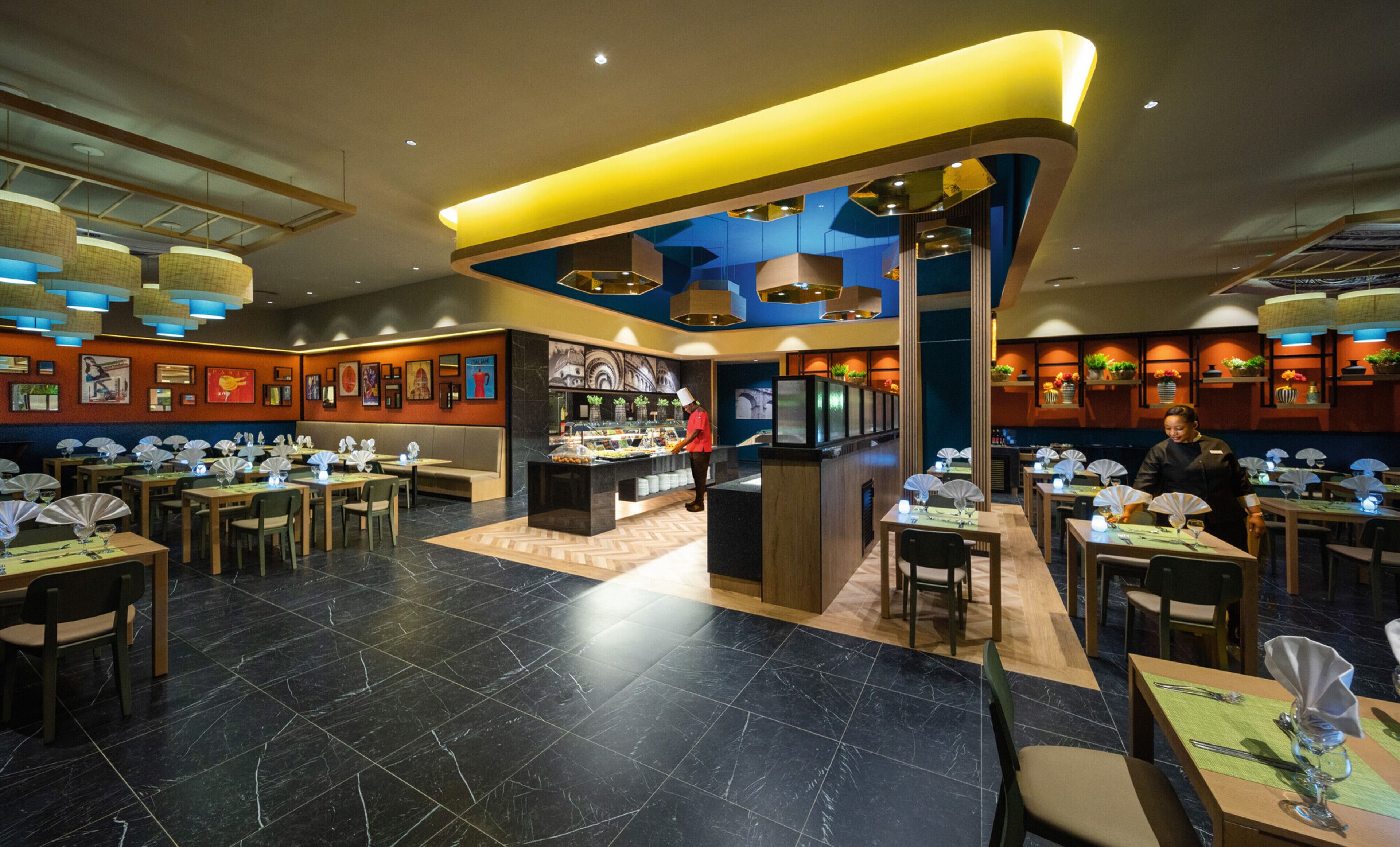 A modern restaurant with a central bar area, multiple dining tables, and a variety of wall decorations.