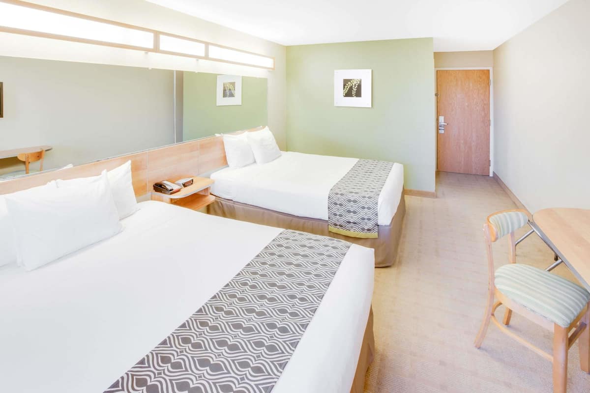 Une chambre d’hôtel avec deux lits, un bureau, une chaise et une porte.