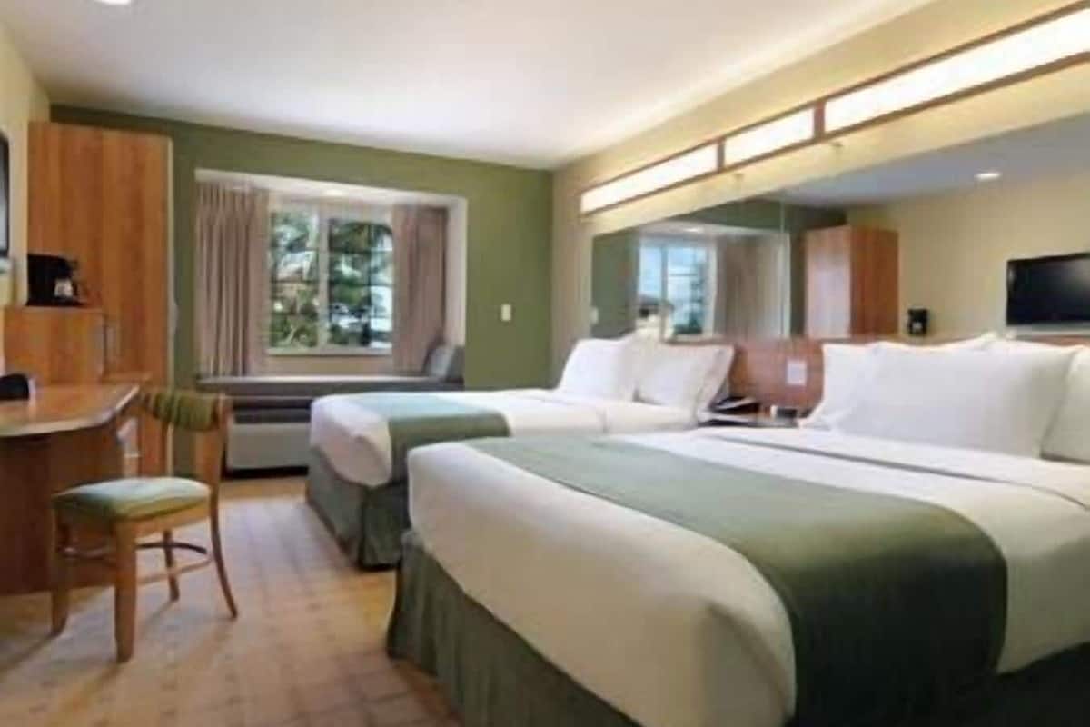Une chambre d’hôtel avec deux lits, un bureau, une chaise et un téléviseur.