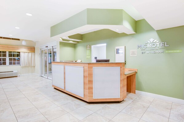 A reception desk in a hotel lobby with a green wall and a sign reading "MICROTEL BY WYNDHAM". - Microtel Inn & Suites by Wyndham Saraland/North Mobile (Saraland)