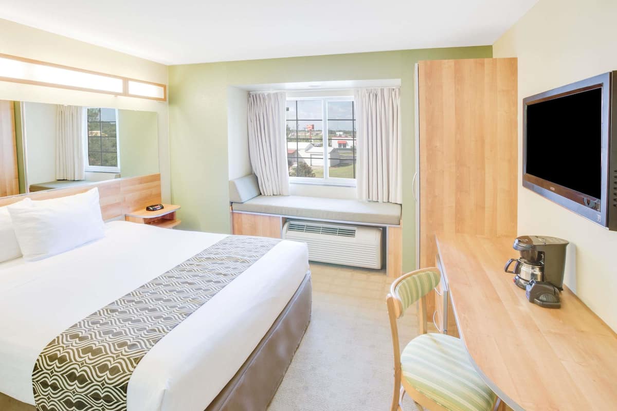 Une chambre d’hôtel avec un lit, un bureau doté d’une machine à café, une chaise, une fenêtre avec des rideaux et un téléviseur fixé au mur.